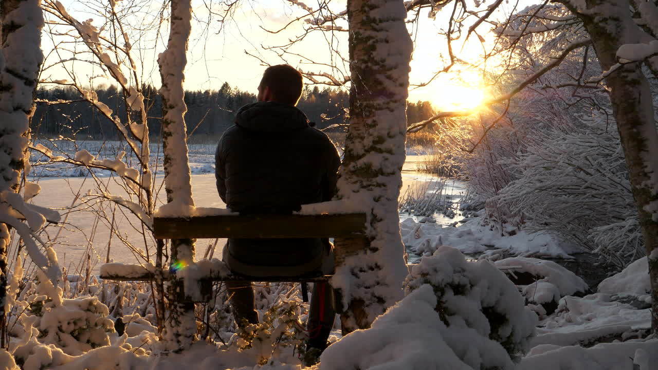 Lone man relaxing in snowy winter wonderland enjoying golden sunset
