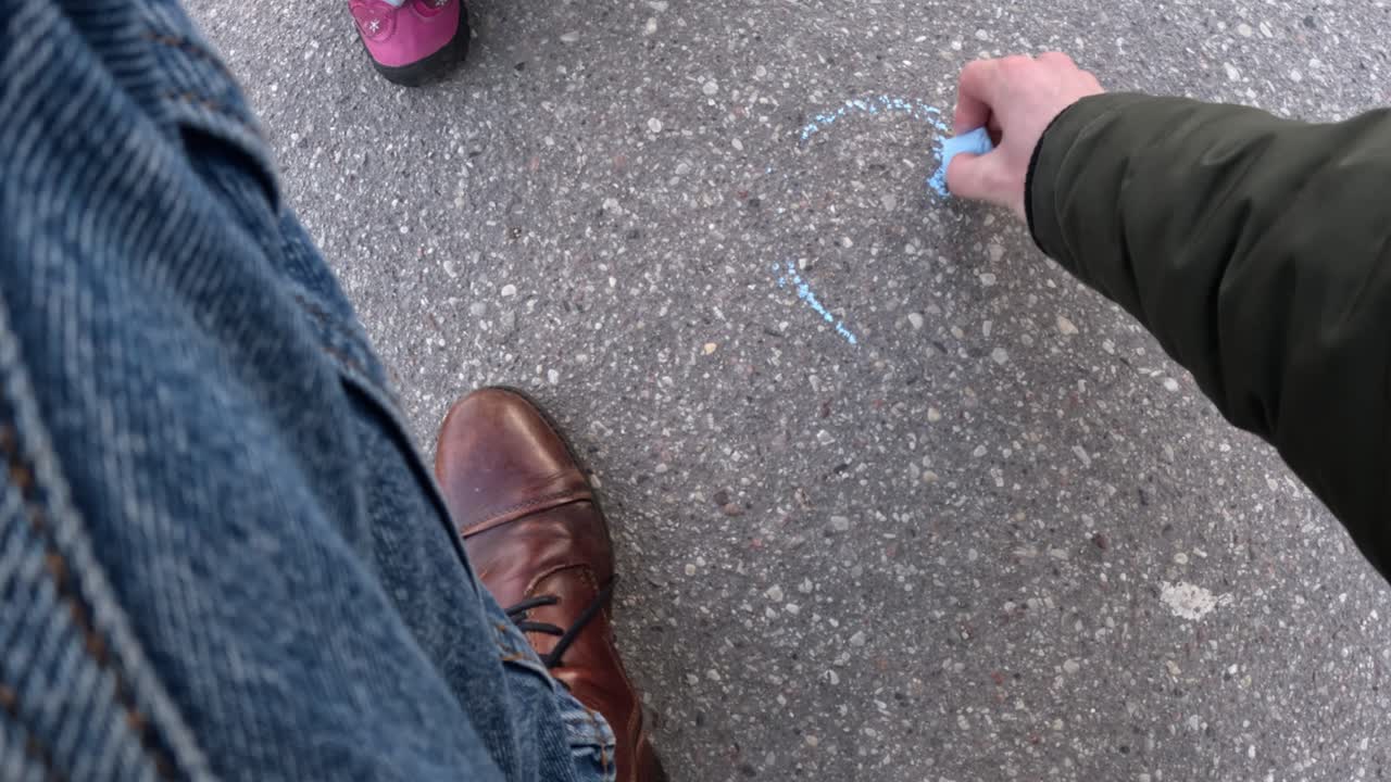 A parent’s perspective as they paint a blue heart on the asphalt, creating a heartfelt moment of creativity and care.