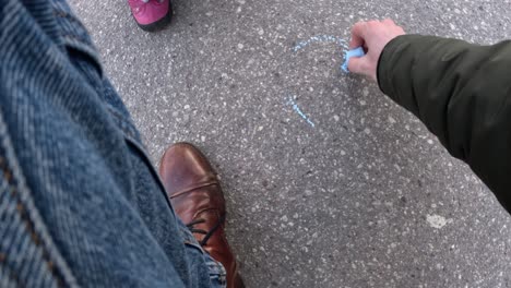 a parent’s perspective as they paint a blue heart on the asphalt, creating a heartfelt moment of creativity and care.
