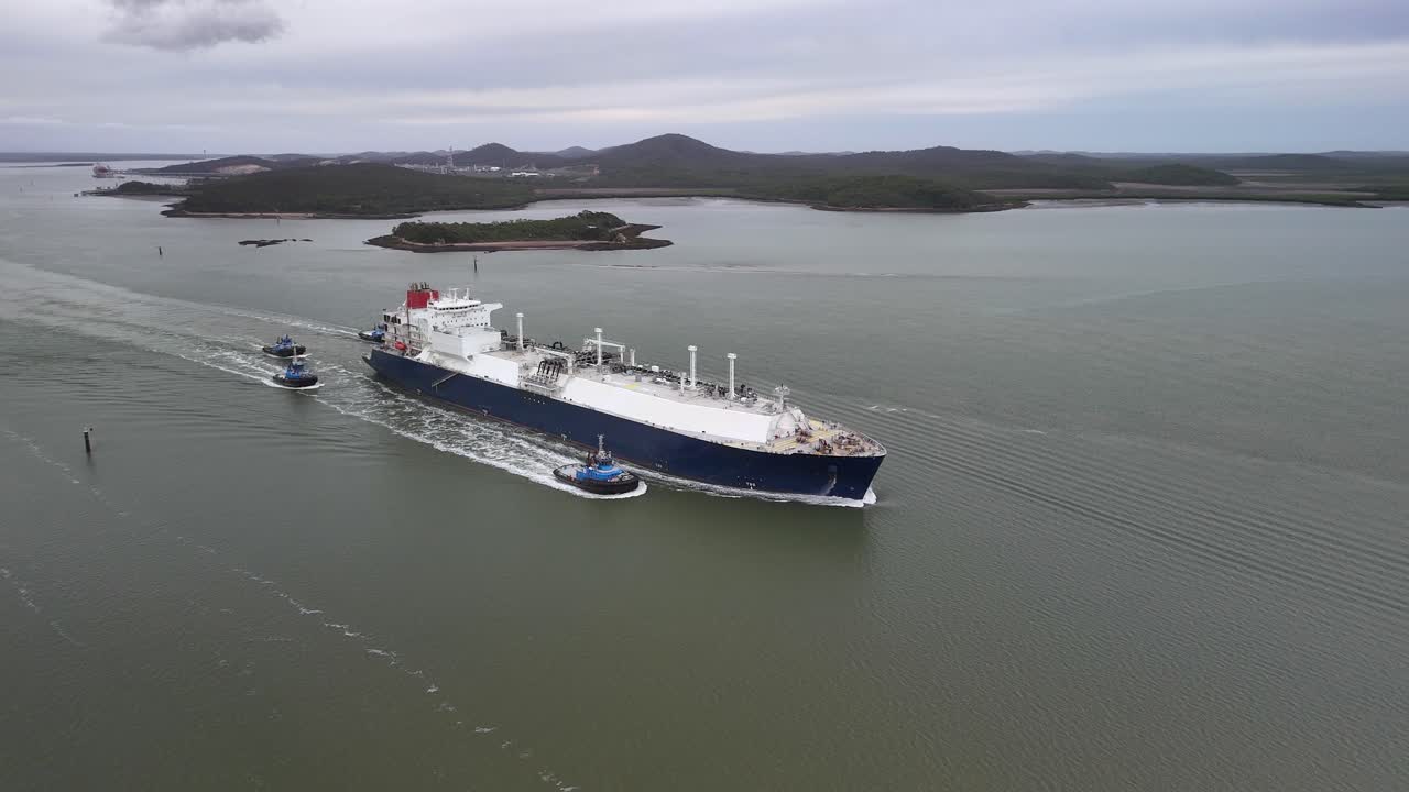 Freighter ship leaves port accompanied by four tug boats in flat light