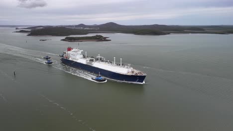 freighter ship leaves port accompanied by four tug boats in flat light