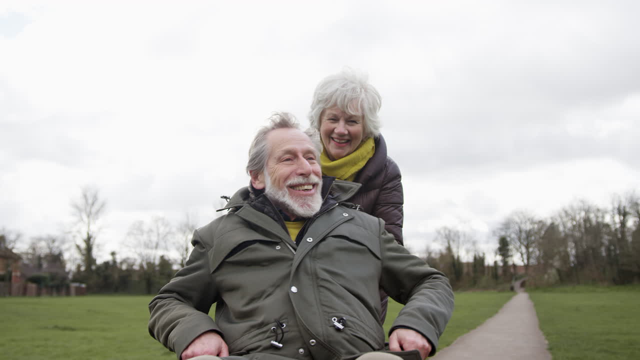 Donna anziana che spinge un uomo anziano in sedia a rotelle all'aperto in un parco autunnale o invernale.