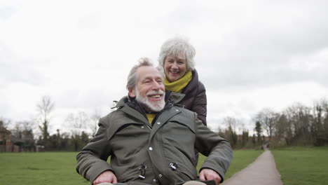 senior woman pushing senior man in wheelchair outdoors in fall or winter park