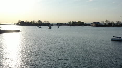 A-low-altitude-drone-view-over-calm-waters,-as-the-camera-dolly-in-and-pan-left-towards-anchored-sailboats-and-an-island,-taking-in-this-sunny,-peaceful-morning