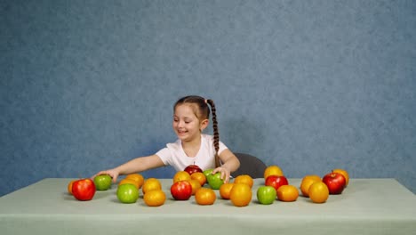 cheerful little girl playing with ripe fruits on the table. happy child building a tower with fresh organic apples. healthy fruits full of vitamins on the table.
