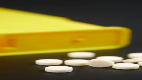 white pills scattered on a dark surface next to a yellow pill dispenser