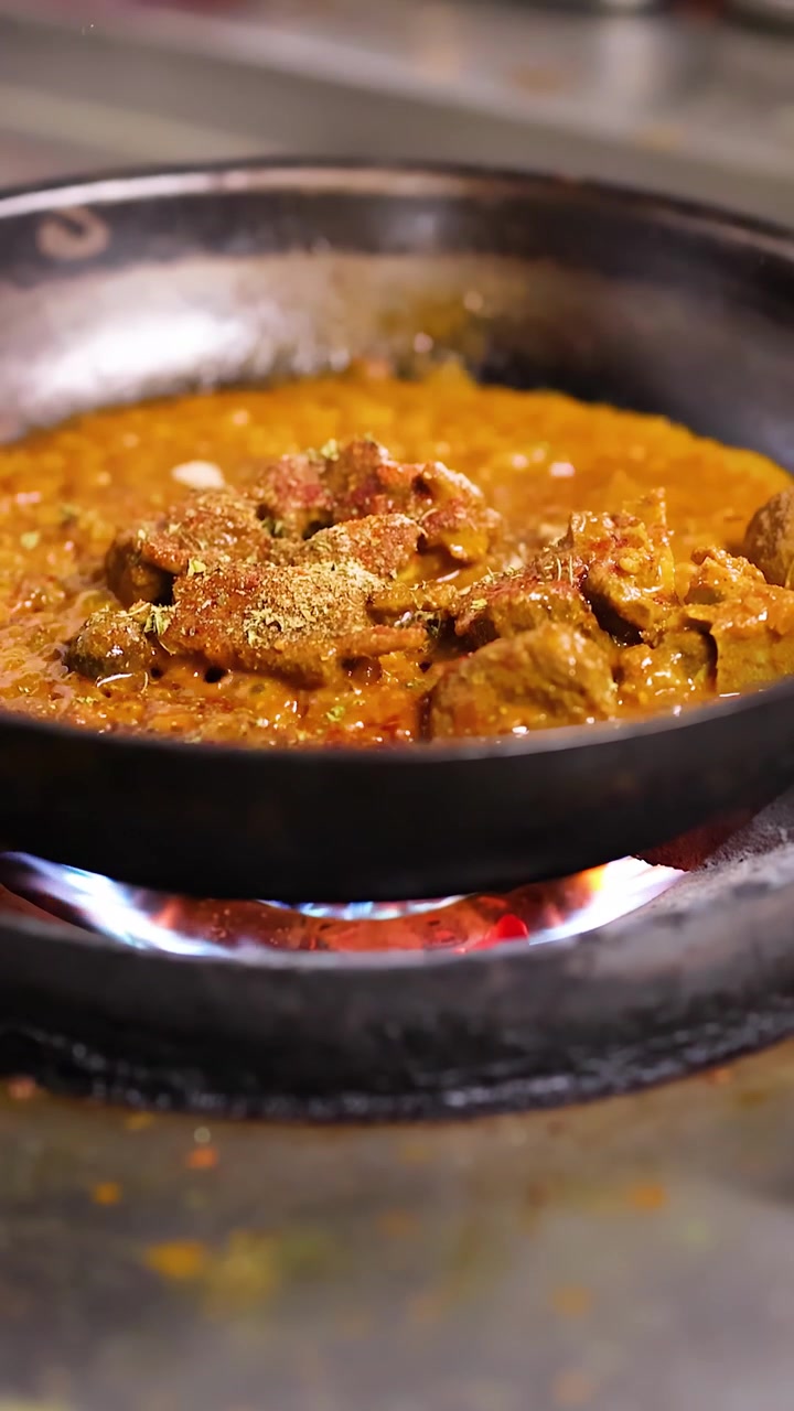 Primo piano di curry di carne che sobbolle in una padella su una fiamma a gas blu.