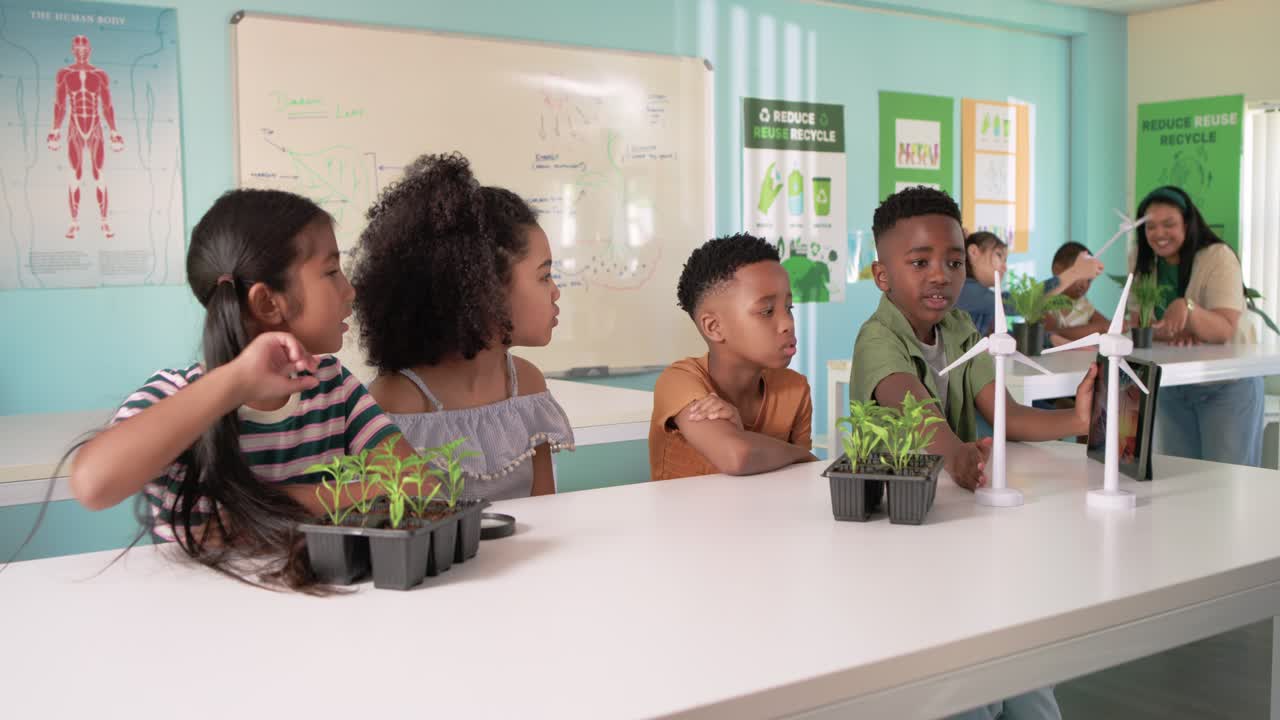 Diverse children leaning as boy shifting tablet toward turbines, touching seedlings for lab demo