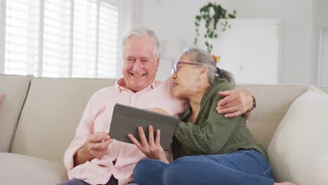 happy diverse senior couple using tablet and sitting on couch
