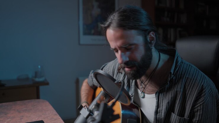 Uomo che canta e suona la chitarra acustica in studio casalingo