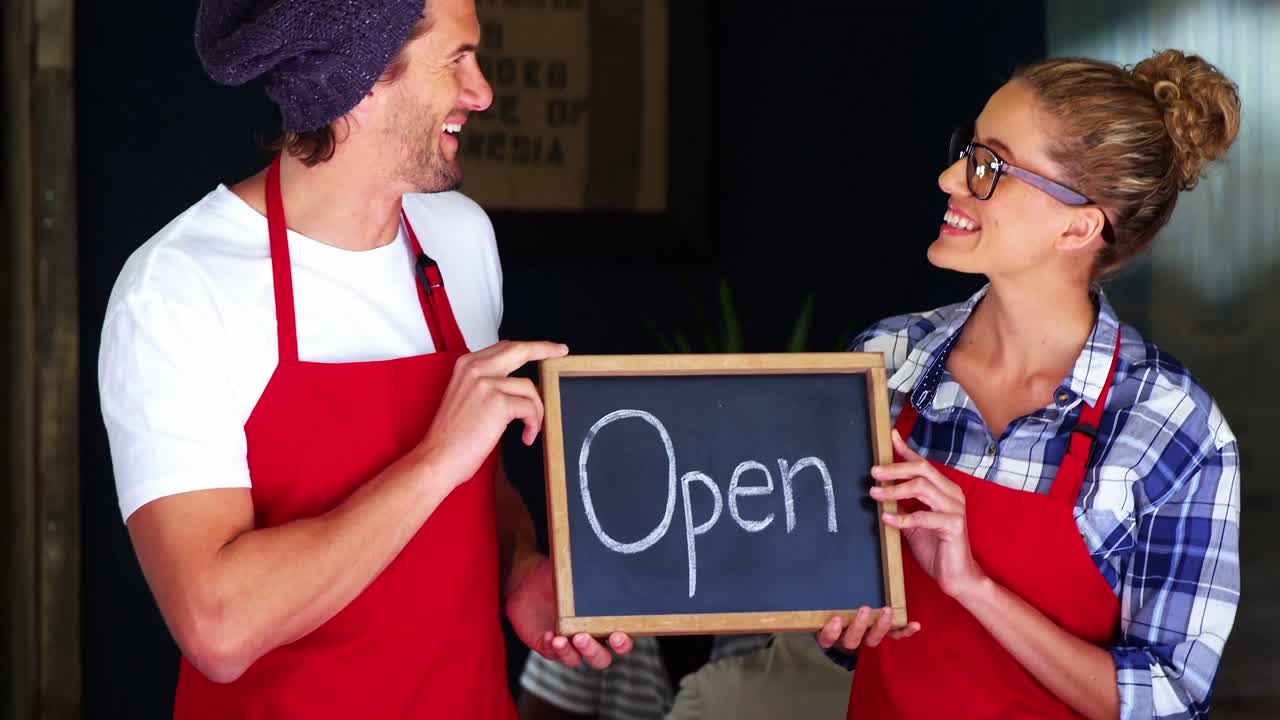Smiling waiter and waitresses holding open sign board
