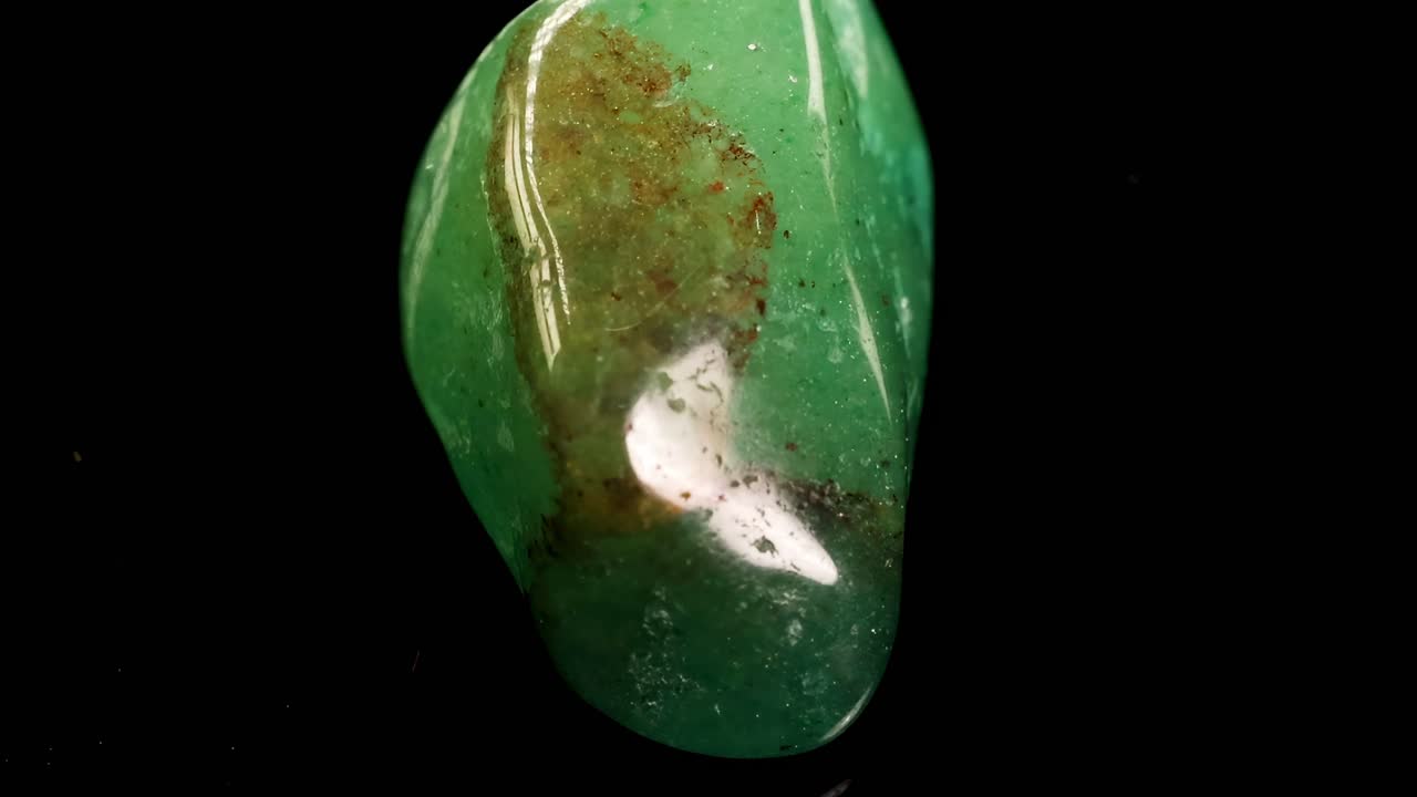 Detailed view of glossy green aventurine stones arranged against a black background, showcasing their natural patterns.