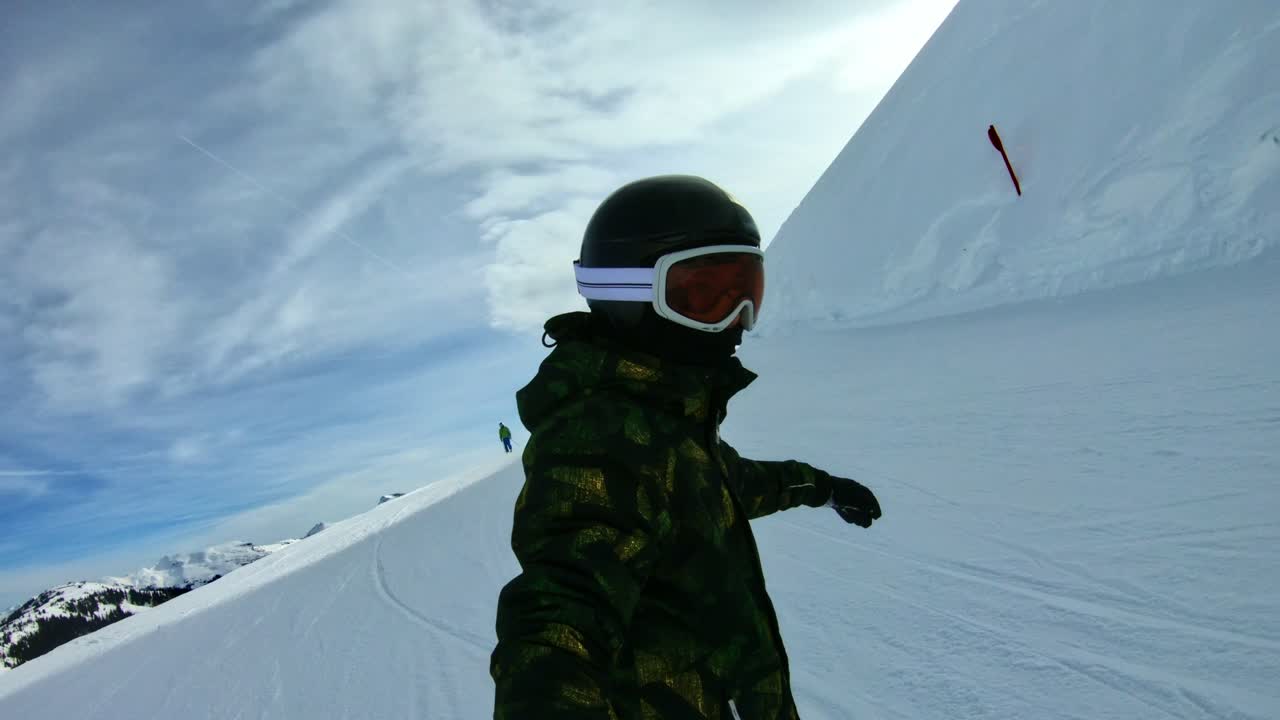 Un bambino che scende con lo snowboard lungo il pendio tenendo in mano un bastone da selfie.