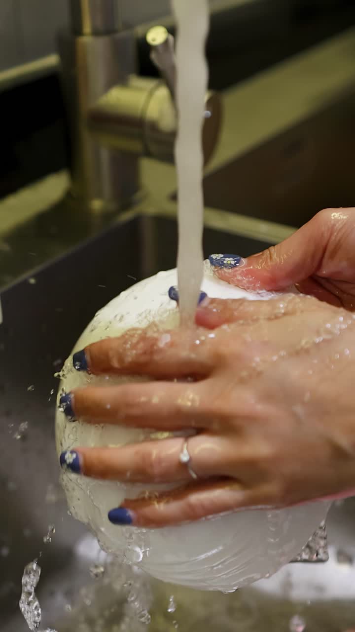 Primo piano di mani che lavano una ciotola di ceramica bianca sotto acqua corrente in un lavello