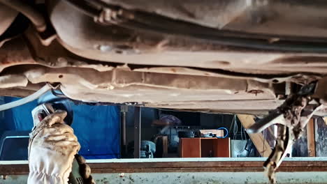 sparks fly as a mechanic uses a grinder under a lifted car in workshop