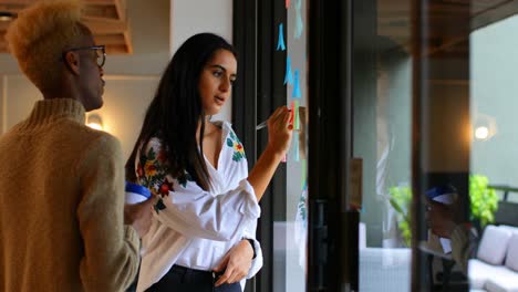 Side-view-of-young-mixed-race-business-colleagues-discussing-over-sticky-notes-in-modern-office-4k