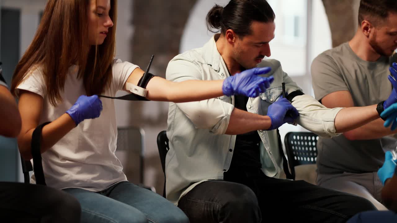 A group of people perform practical exercises in medicine to provide first aid. Nurse in white medical uniform helps man tighten medical tourniquet on arm