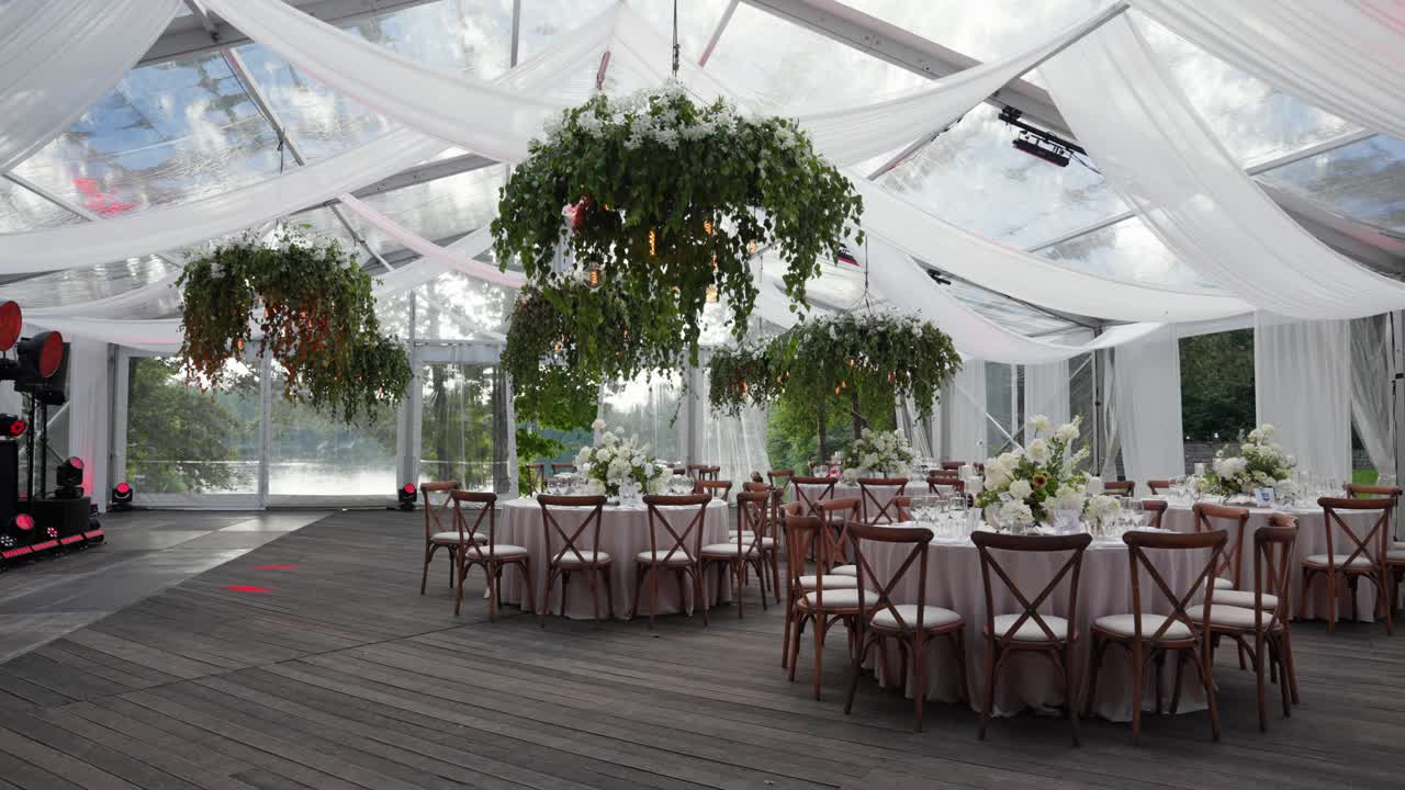 Captivating wedding venue with exquisite table settings. Lush greenery suspended from a transparent ceiling casts soft shadows, creating an enchanting atmosphere perfect for celebrations