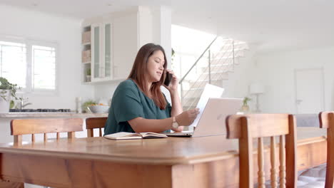 Plus-size-biracial-woman-with-document,-talking-on-phone-and-using-laptop,-copy-space,-slow-motion