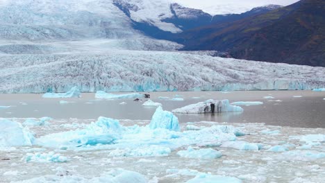 iceberg azul turquesa derritiéndose, al fondo el glaciar y sus montañas de islandia