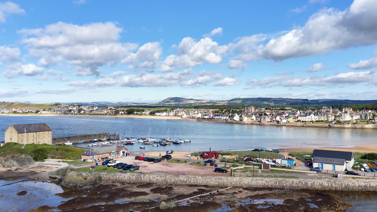 Drone camera smoothly pans across Fife harbor, waterfront, and village under bright daylight skies
