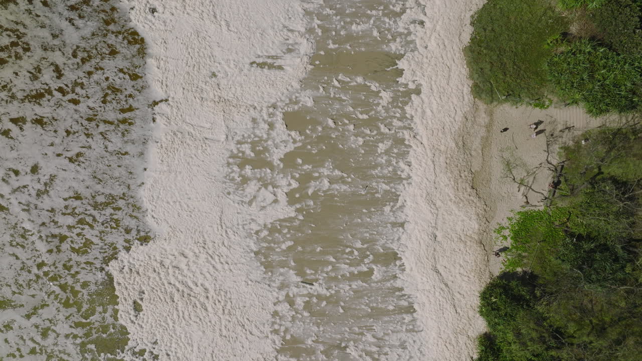 tomada aérea de 4k de arriba hacia abajo en movimiento lento de una playa australiana con espuma marina, espuma oceánica, espuma de playa o espuma creada por la agitación del agua de mar