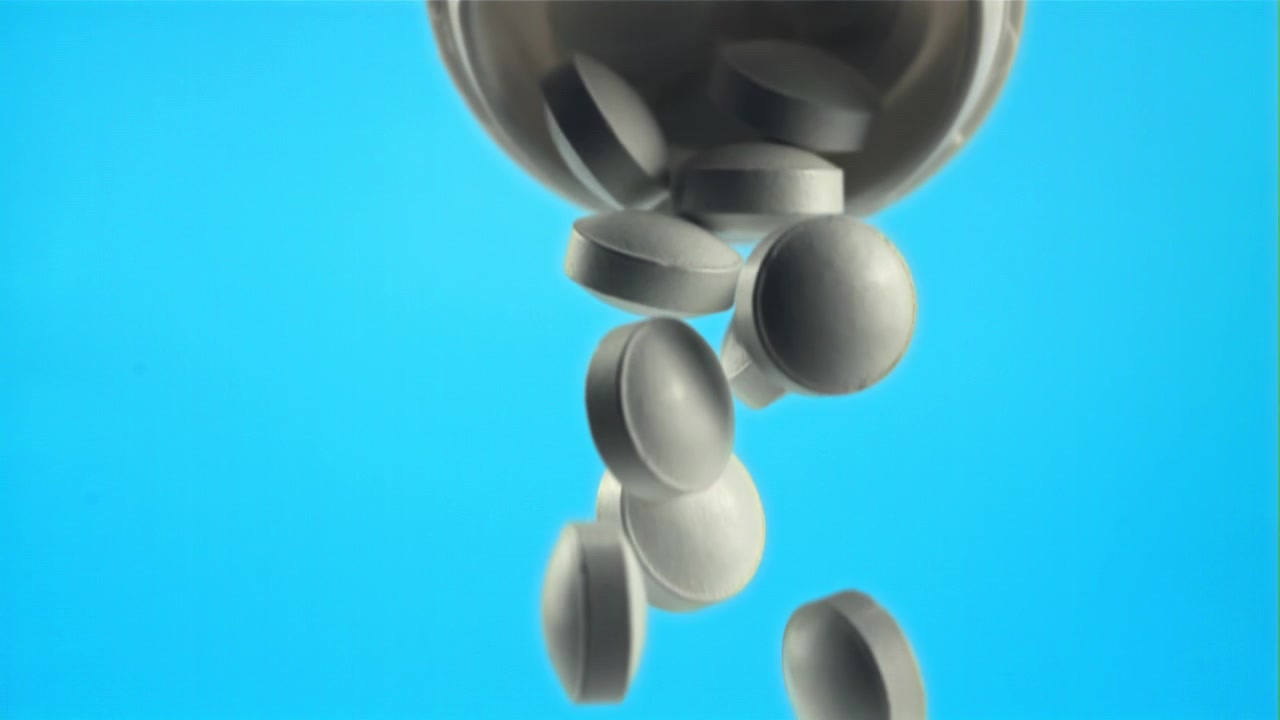 Movimento rallentato di pillole bianche che cadono da un flacone di medicinali