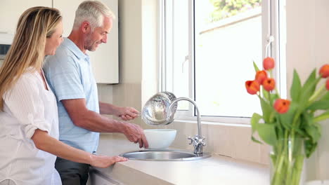 happy couple washing broccoli at the sink