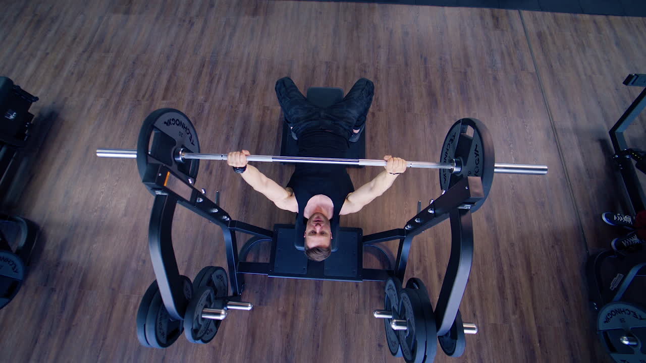 Athletic Bodybuilder Doing Barbell Exercise. Top view of professional athlete doing bench press workout with barbell