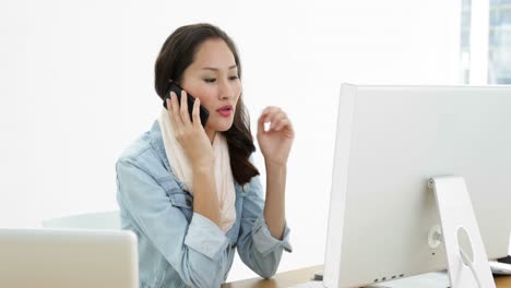 asian woman working at desk using computer talking on the phone