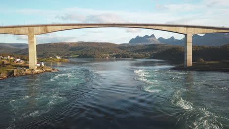 drone shot flying low over the maelstrom saltstraumen, under the bridge and towards the majestic mountains in the background