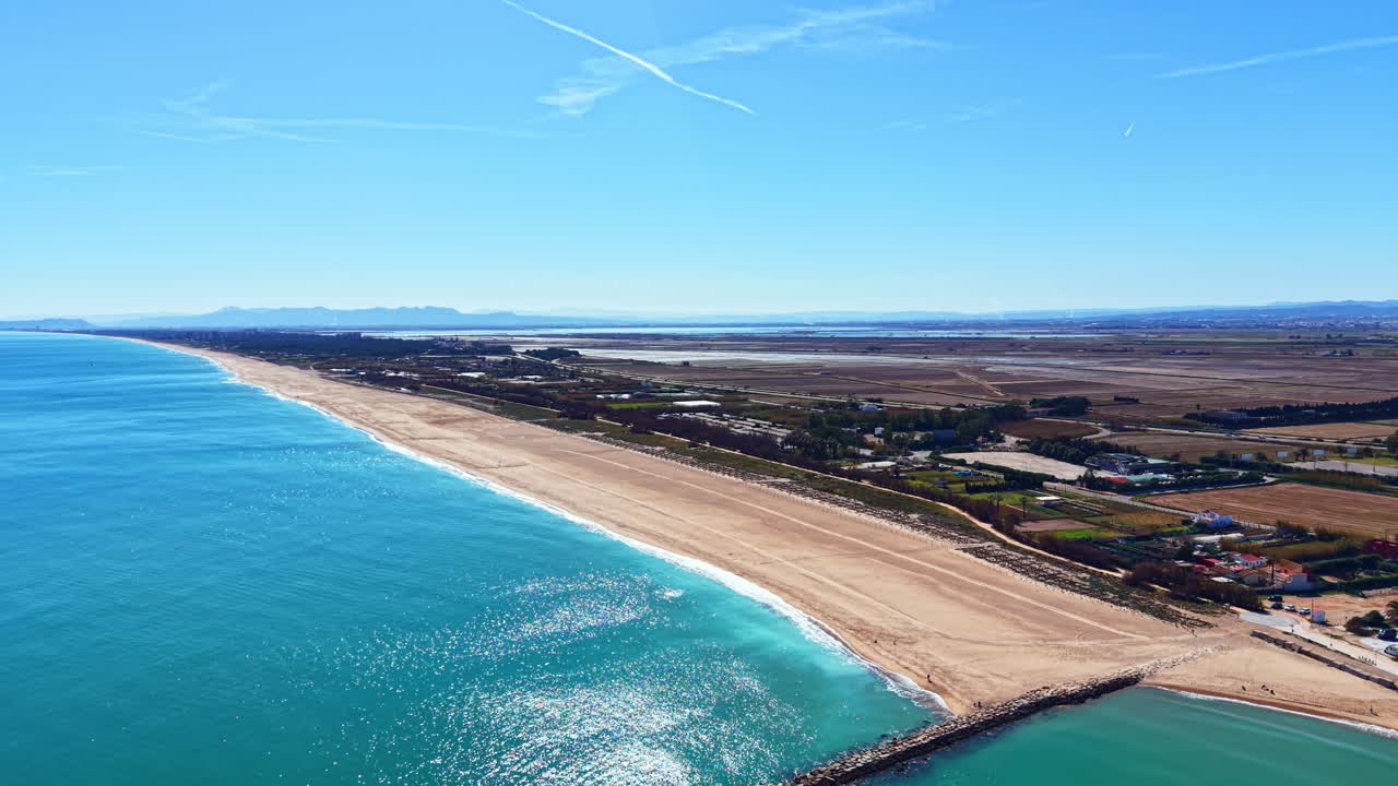 Vista costera de una playa de arena y aguas cristalinas en España durante un día soleado y brillante, con tierra distante a la vista
