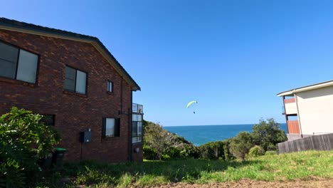 a paramotor flies over a coastal house