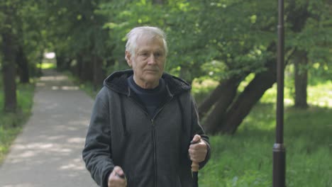 active senior old man training nordic walking with ski trekking poles in park