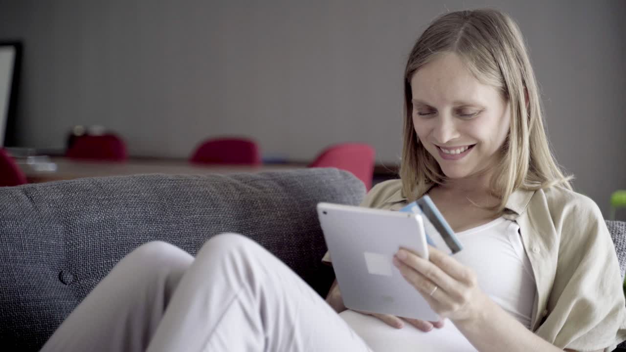 Smiling pregnant woman shopping online with tablet