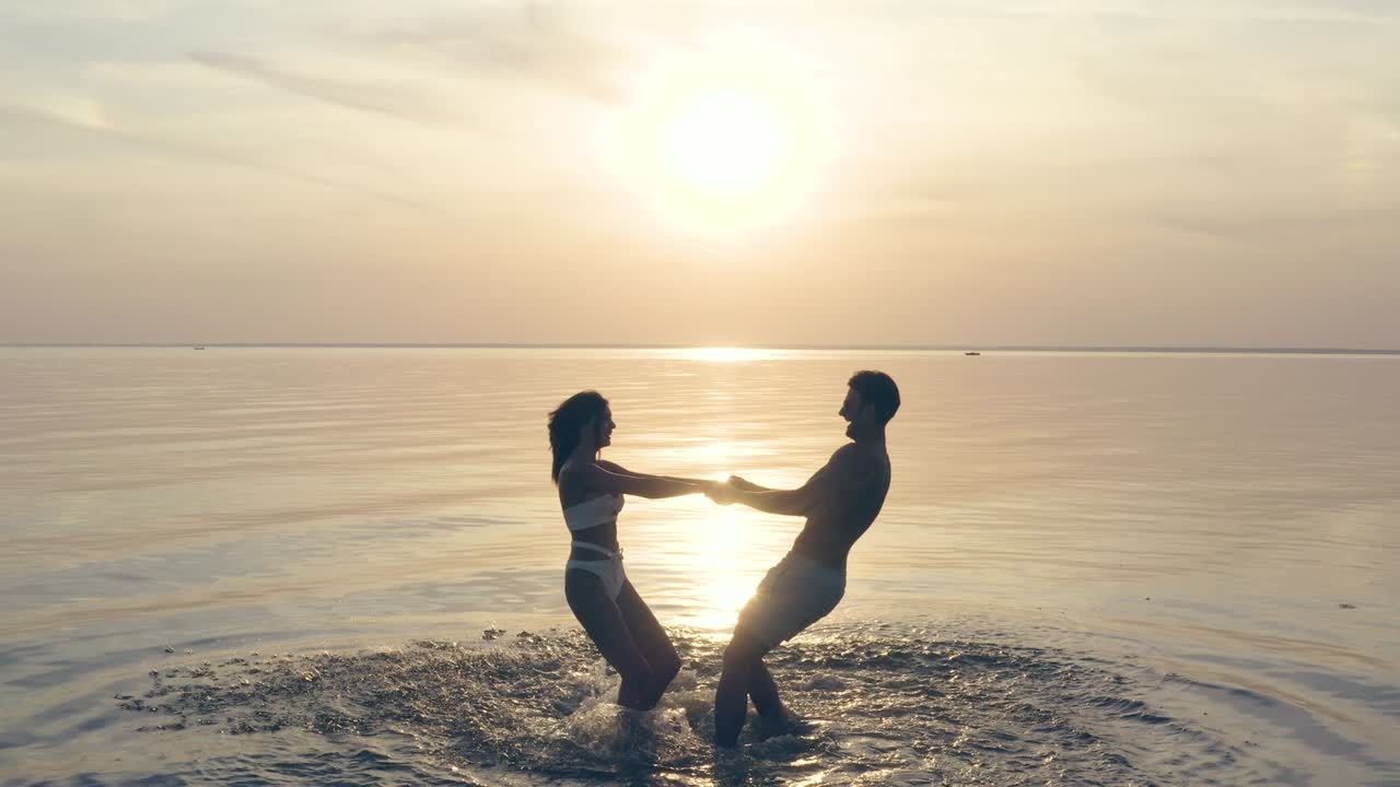 젊은 부부는 손을 잡고 아름다운 일몰을 향해 회전합니다.