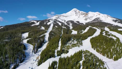 aerial drone shot of big sky shows skiers ascending mountain trails on chair lifts, while others carve down winding snowy runs in a pristine montana alpine resort setting