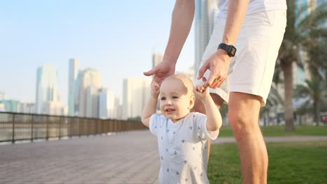 Padre-Joven-Con-Un-Niño-Y-Primeros-Pasos.-Padre-Joven-Con-Un-Niño-En-El-Aprendizaje-Al-Aire-Libre-Para-Dar-Los-Primeros-Pasos-Cerca-De-Una-Casa-Urbana-En-La-Ciudad