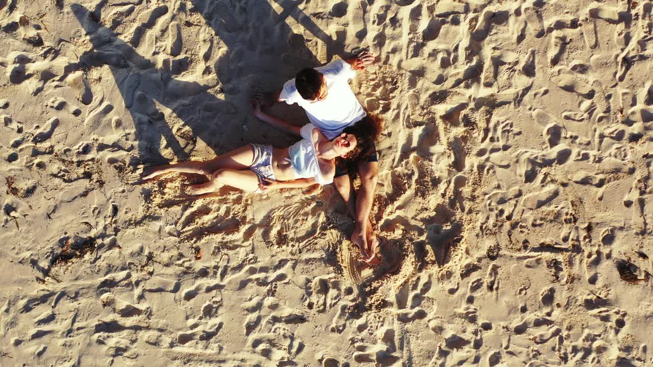 Couple in love lying on soft sand with traces of footprints around, exotic beach under first rays of sunrise in tropical island of Antigua