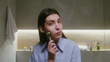 woman using jade roller for facial massage in bathroom