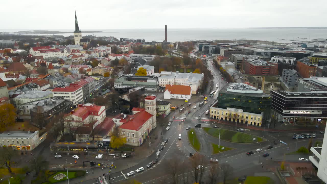 Aerial drone footage orbiting Tallinn central city Biru centre small urban roundabout where cars, trams and buses are driving during a autumn wet and cloudy day. Church towers, medieval buildings also