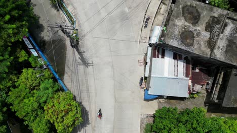 Vista-Aérea-De-Arriba-Hacia-Abajo-De-Una-Calle-Concurrida-En-El-Pueblo-Del-Sudeste-Asiático-En-Los-Trópicos-Con-Ciclomotores-Y-Triciclos-Conduciendo