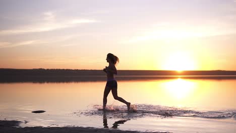 slender woman with long hair running outdoors. jogging by the water. seaside. sun shines on the background