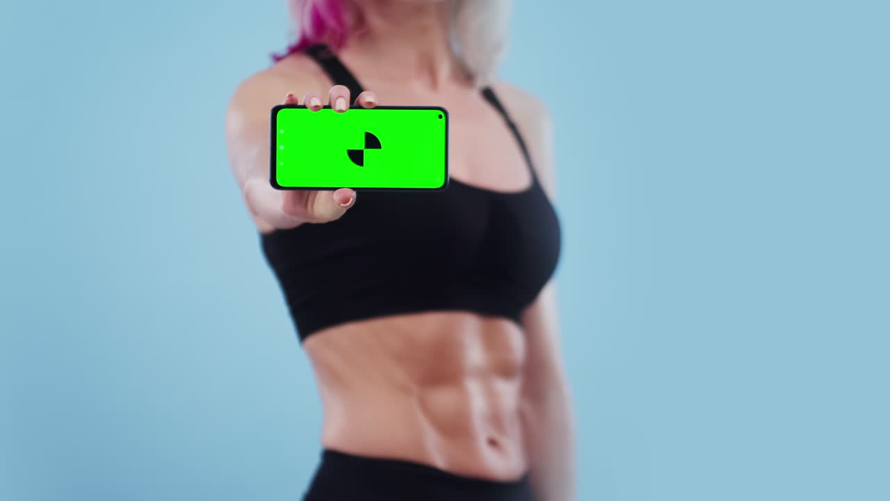 mujer deportiva muestra la pantalla del teléfono con una aplicación en el estudio, pantalla verde. concepto de programa e información para deportes