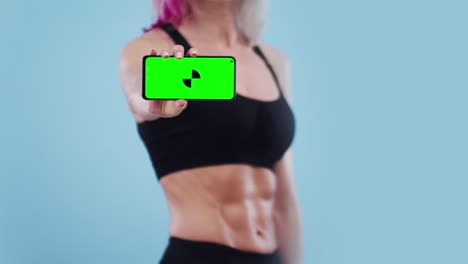mujer deportiva muestra la pantalla del teléfono con una aplicación en el estudio, pantalla verde. concepto de programa e información para deportes