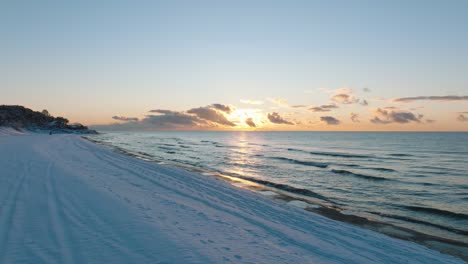 aerial footage of beach covered with snow, sunny winter day at the sunset, golden hour, nordic woodland pine tree forest, baltic sea coast, wide drone shot moving forward low