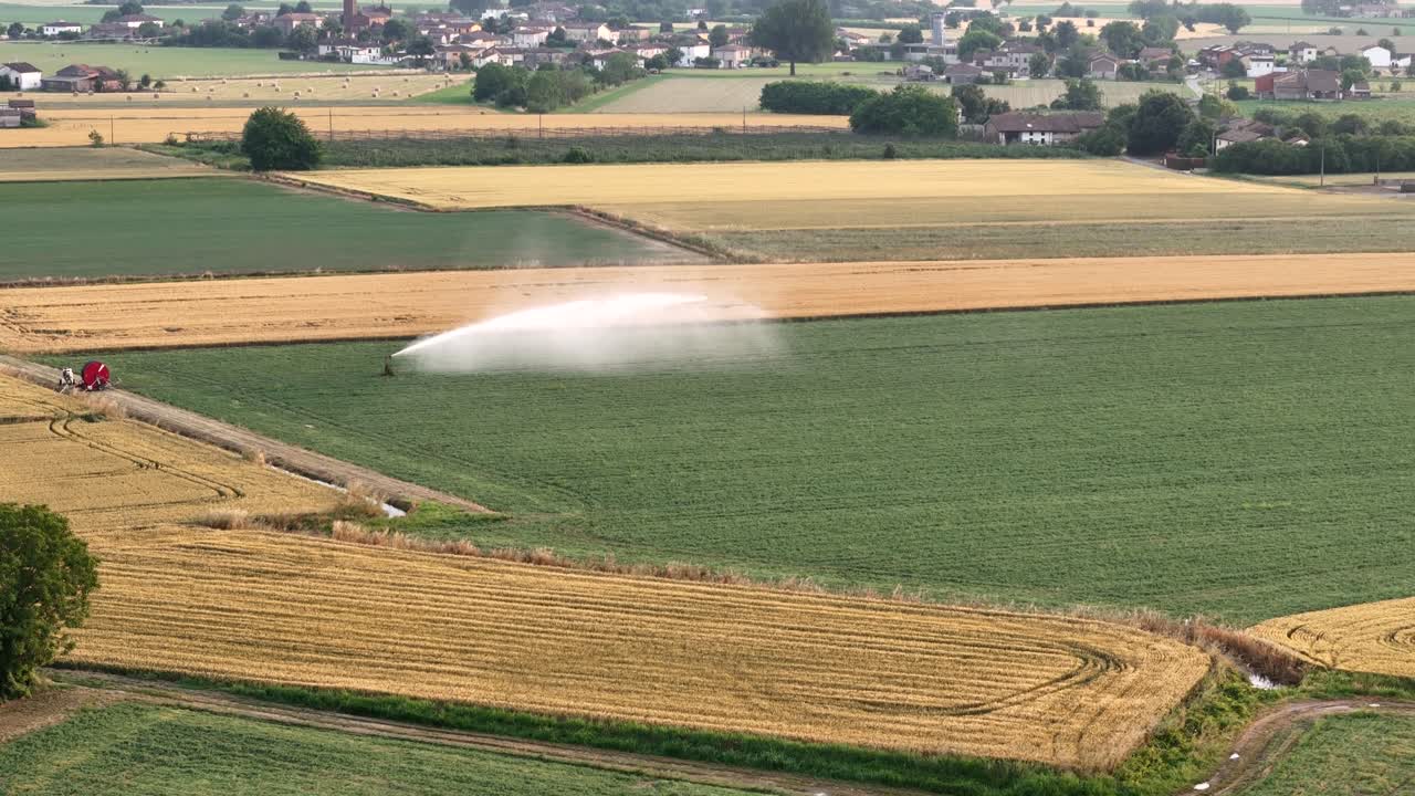 Irrigating soybean farmland under bright sunlight, rural Po Valley landscape featuring traditional houses, lush agricultural scenery in northern Italy, aerial push in shot