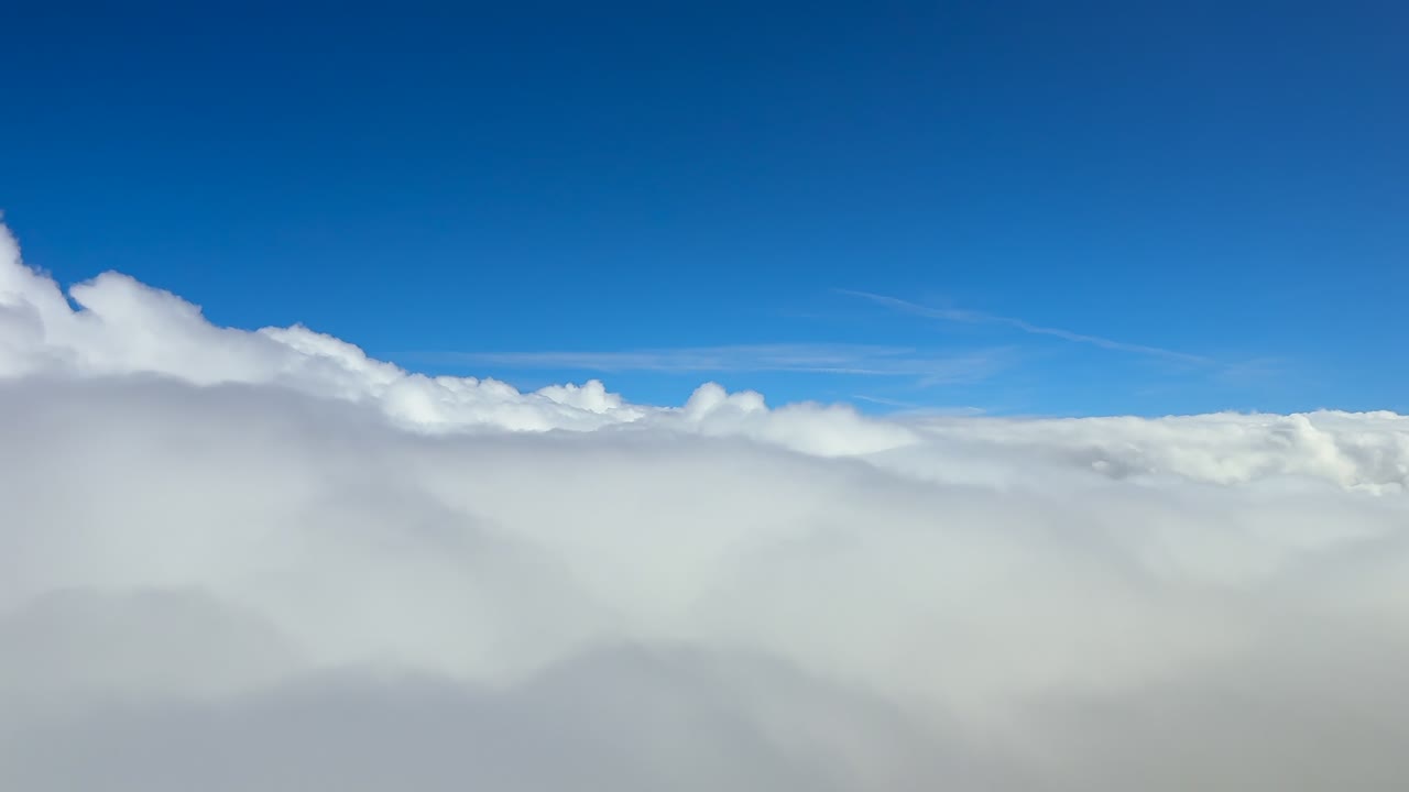 A pilot’s perspective from a jet cockpit in a smooth flight above and into an endless sea of white fluffy stratus clouds under a deep blue color sky. Ultra-realistic 4K shot