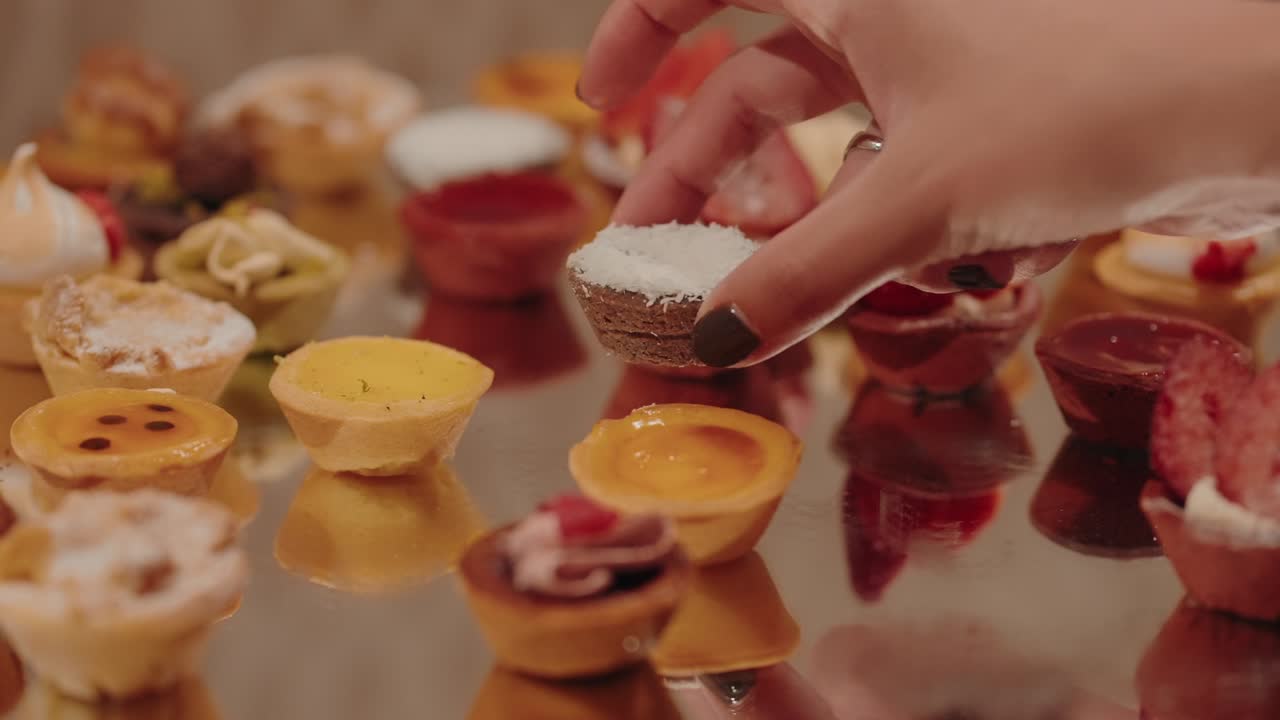 hand picks colorful mini tarts on reflective dessert surface