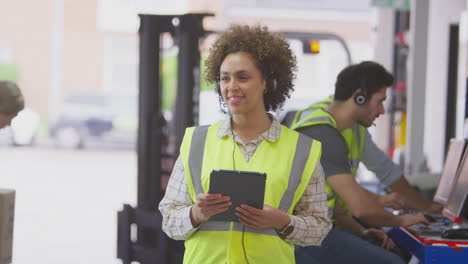 female manager wearing headset in logistics distribution warehouse using digital tablet